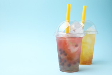 Photo of Tasty bubble tea in plastic cups on light blue background, space for text