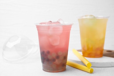 Tasty bubble tea in plastic cups and straws on light table, closeup