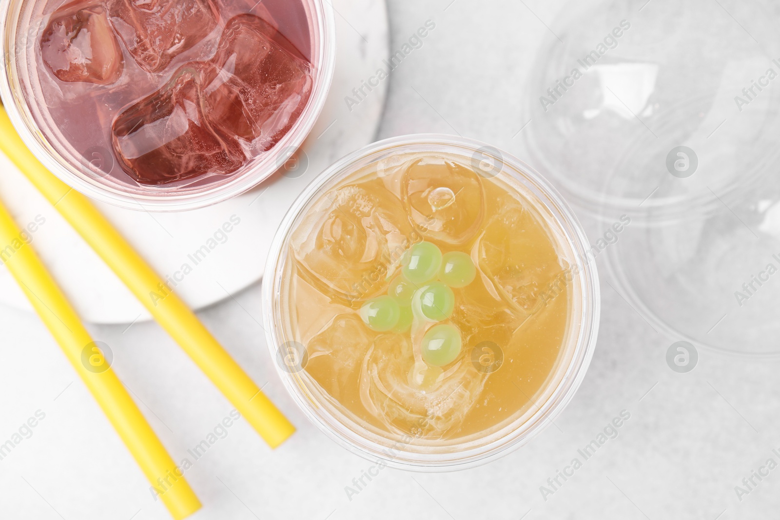 Photo of Tasty bubble tea in plastic cups and straws on light table, flat lay