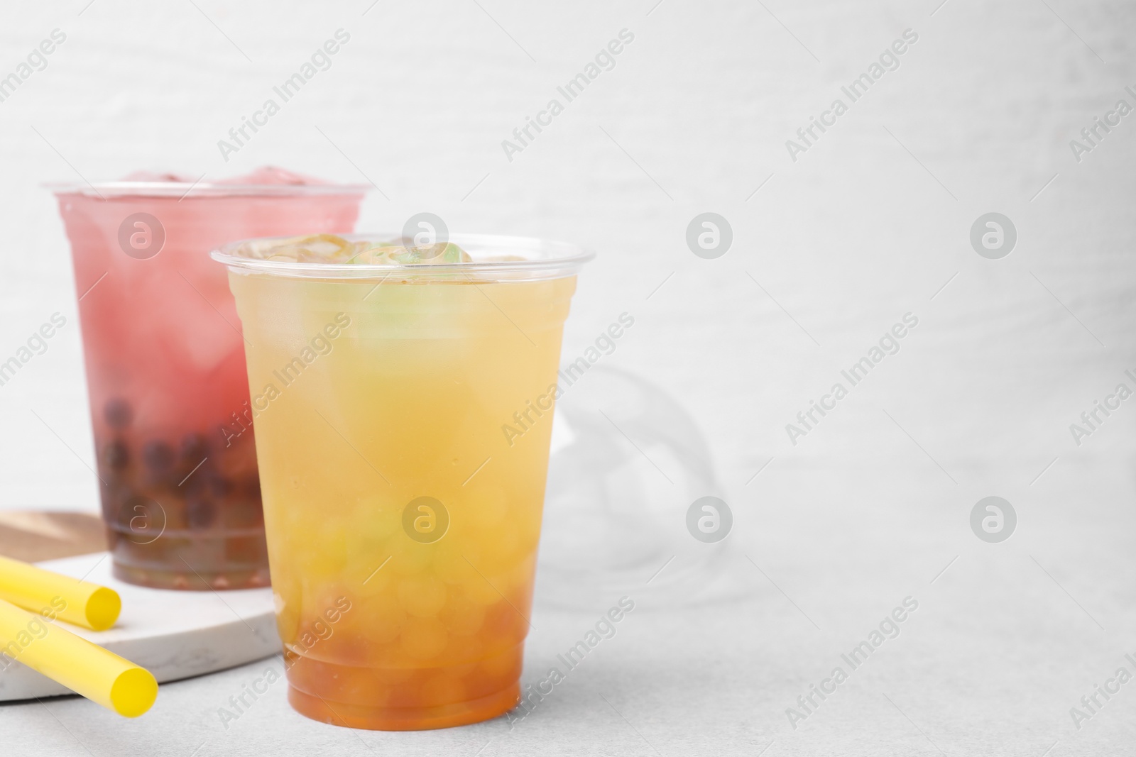 Photo of Tasty bubble tea in plastic cups and straws on light table, space for text