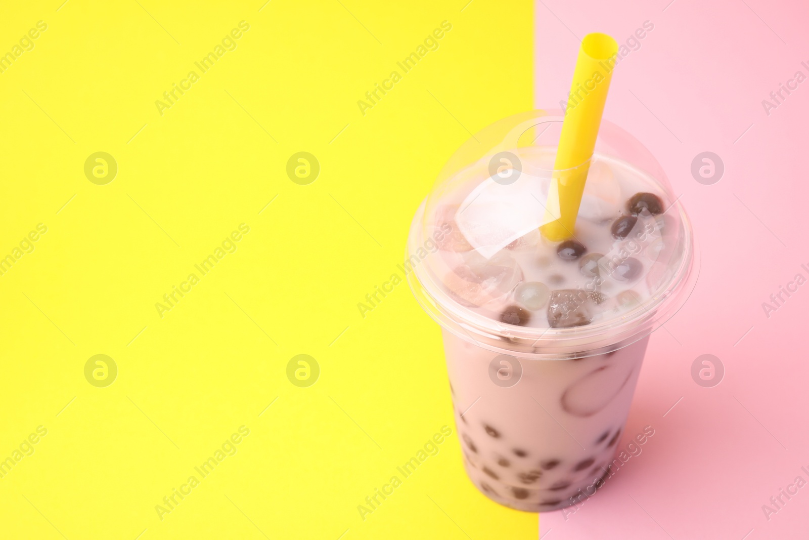 Photo of Tasty milk bubble tea in plastic cup on color background, space for text