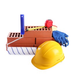 Photo of Yellow hard hat, red bricks, gloves, roller and measuring tape isolated on white. Building material and construction tools