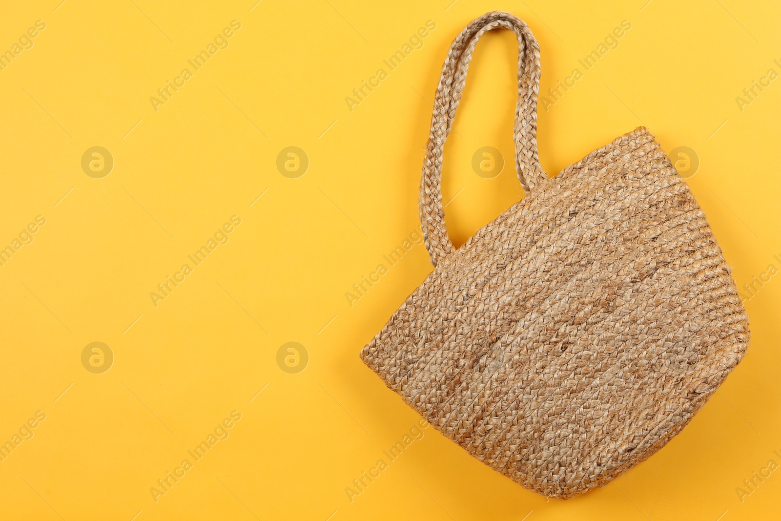 Photo of Stylish woman's straw bag on yellow background, top view. Space for text