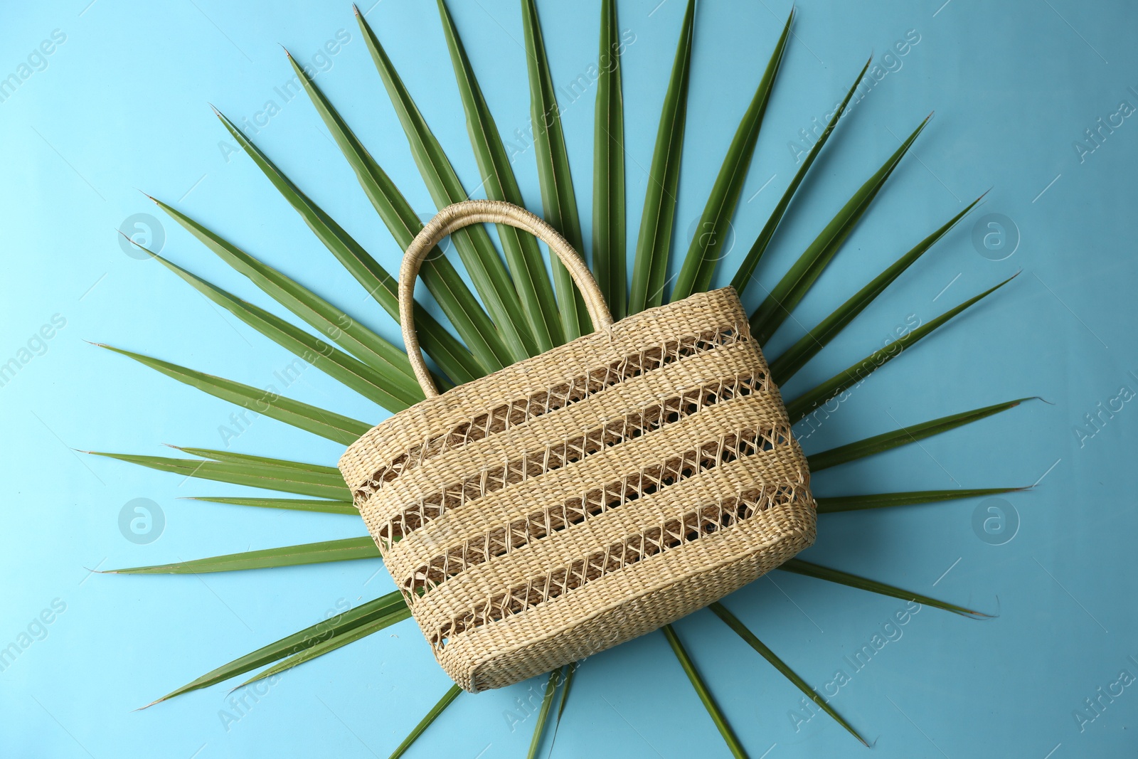 Photo of Elegant woman's straw bag with tropical leaf on light blue background, top view