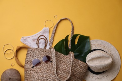 Photo of Stylish straw bag and summer accessories on yellow background, flat lay