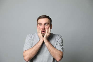 Young man feeling fear on grey background