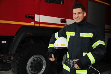 Photo of Portrait of firefighter in uniform with helmet near fire truck at station, space for text