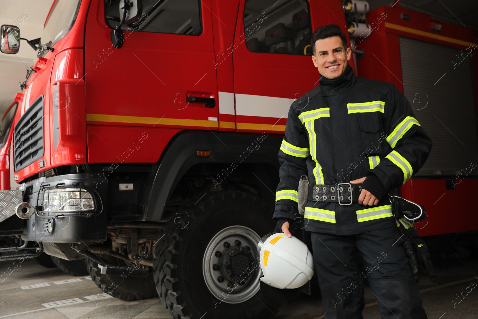 Photo of Portrait of firefighter in uniform with helmet near fire truck at station, space for text