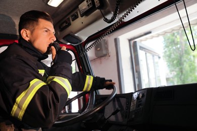 Firefighter using radio set while driving fire truck, space for text