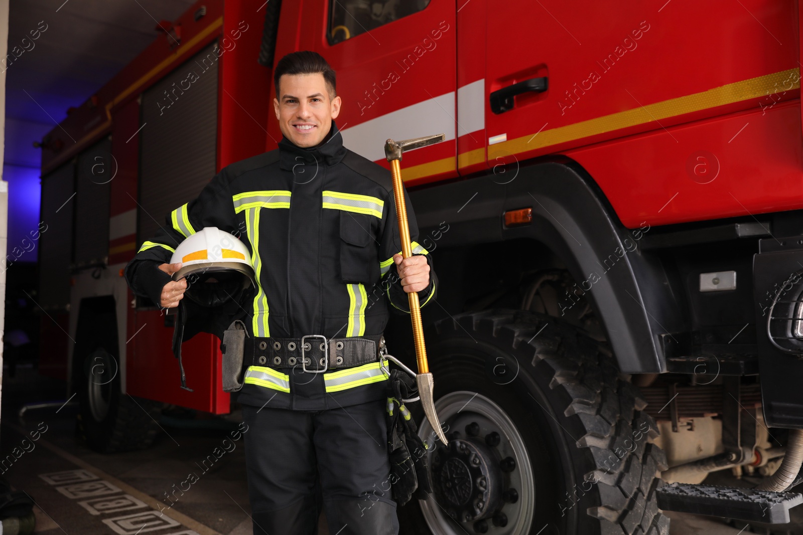 Photo of Portrait of firefighter in uniform with helmet and entry tool near fire truck at station