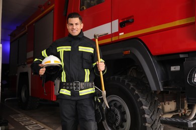 Portrait of firefighter in uniform with helmet and entry tool near fire truck at station