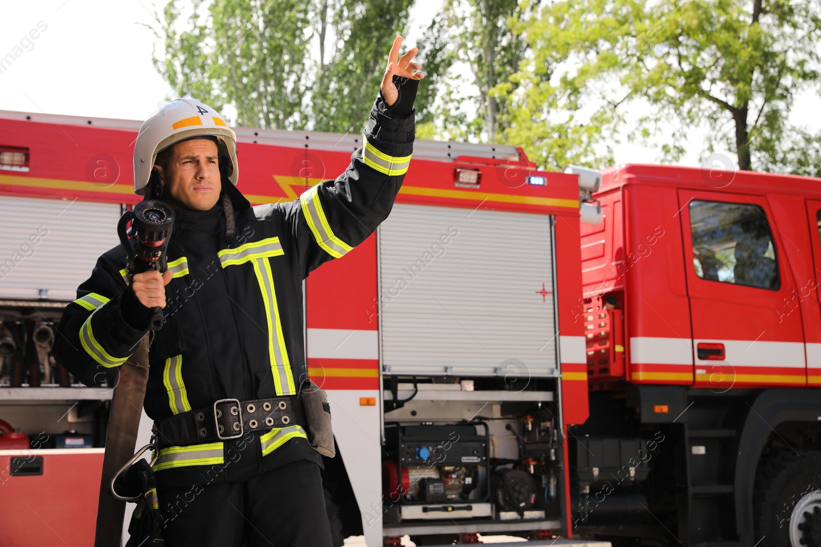 Photo of Firefighter in uniform with high pressure water jet near fire truck outdoors