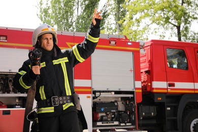 Photo of Firefighter in uniform with high pressure water jet near fire truck outdoors