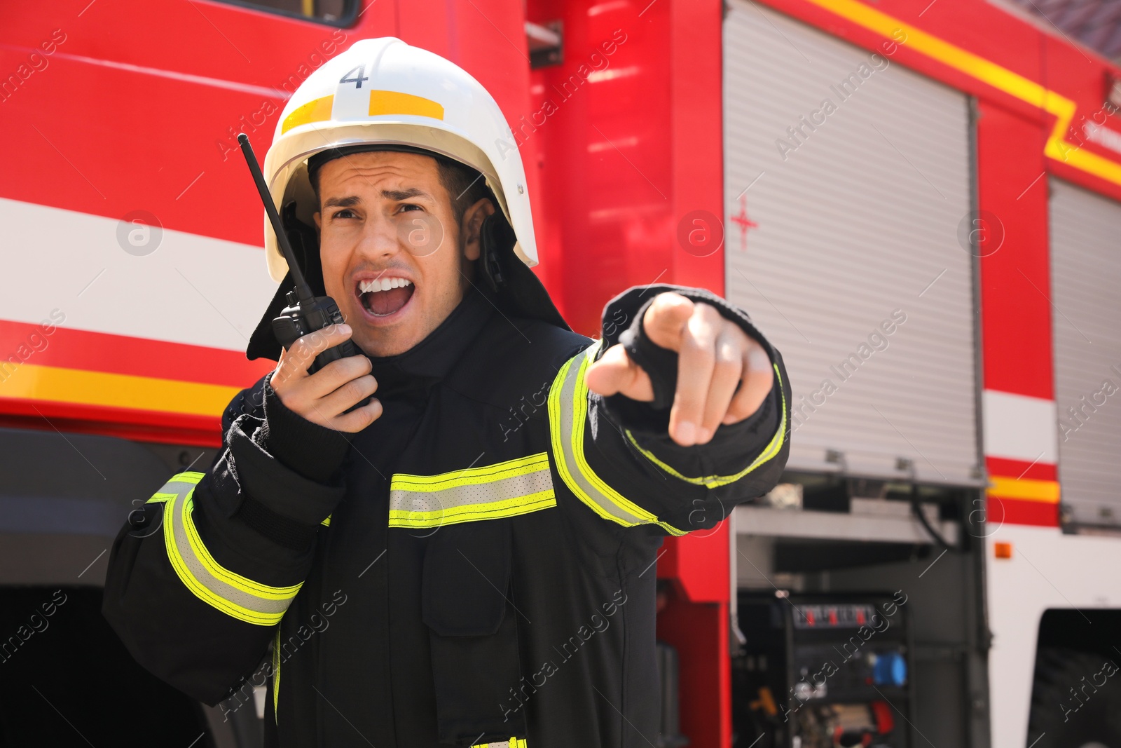 Photo of Firefighter in uniform using portable radio set near fire truck outdoors