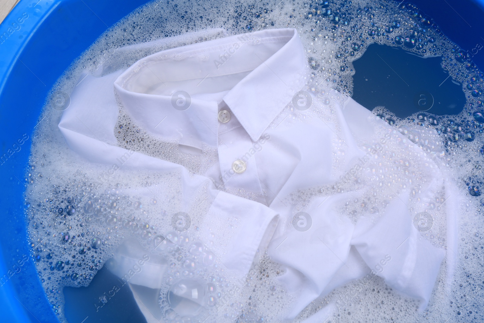 Photo of White shirt in suds, closeup. Hand washing laundry