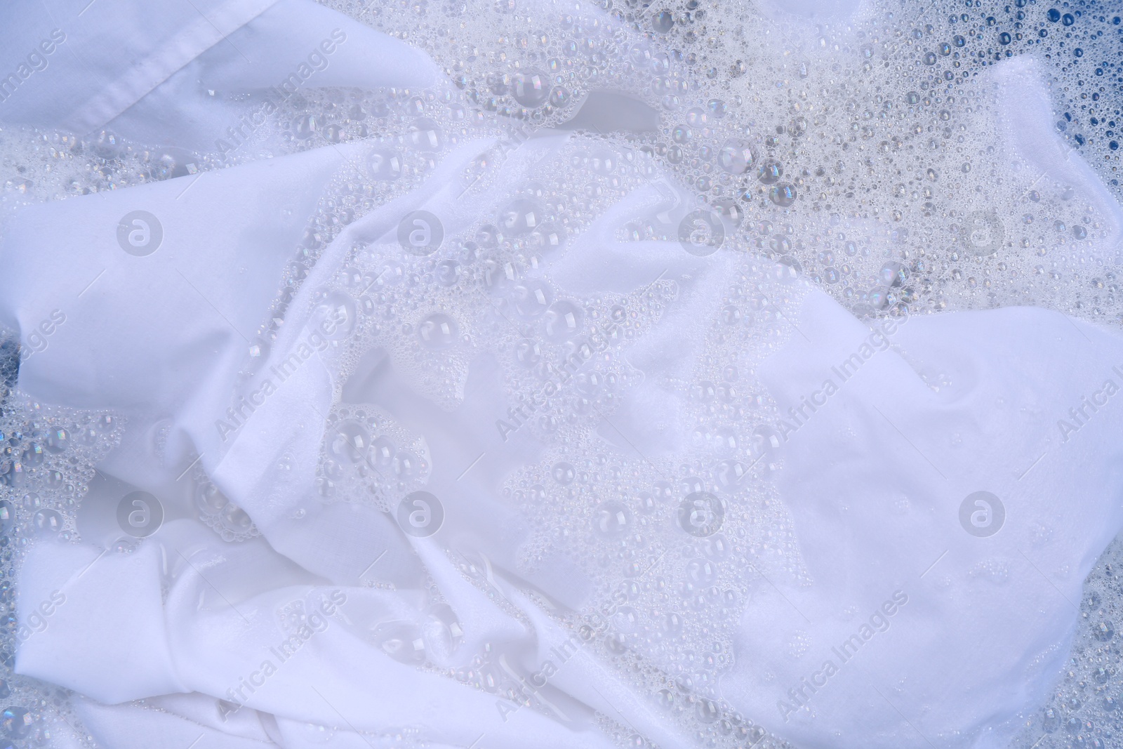 Photo of White garment in suds, closeup. Hand washing laundry