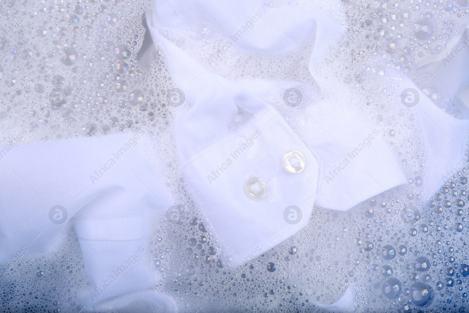 Photo of White garment in suds, closeup. Hand washing laundry