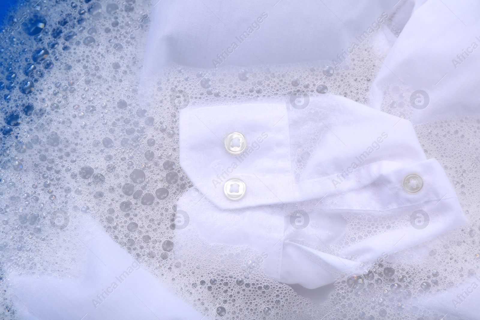 Photo of White garment in suds, closeup. Hand washing laundry