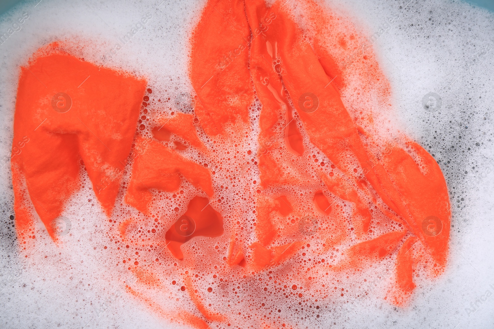 Photo of Orange garment in suds, top view. Hand washing laundry