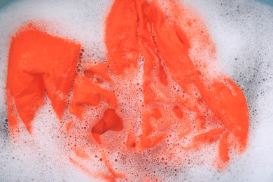 Photo of Orange garment in suds, top view. Hand washing laundry