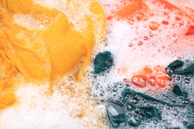 Photo of Colorful clothes in suds, closeup. Hand washing laundry