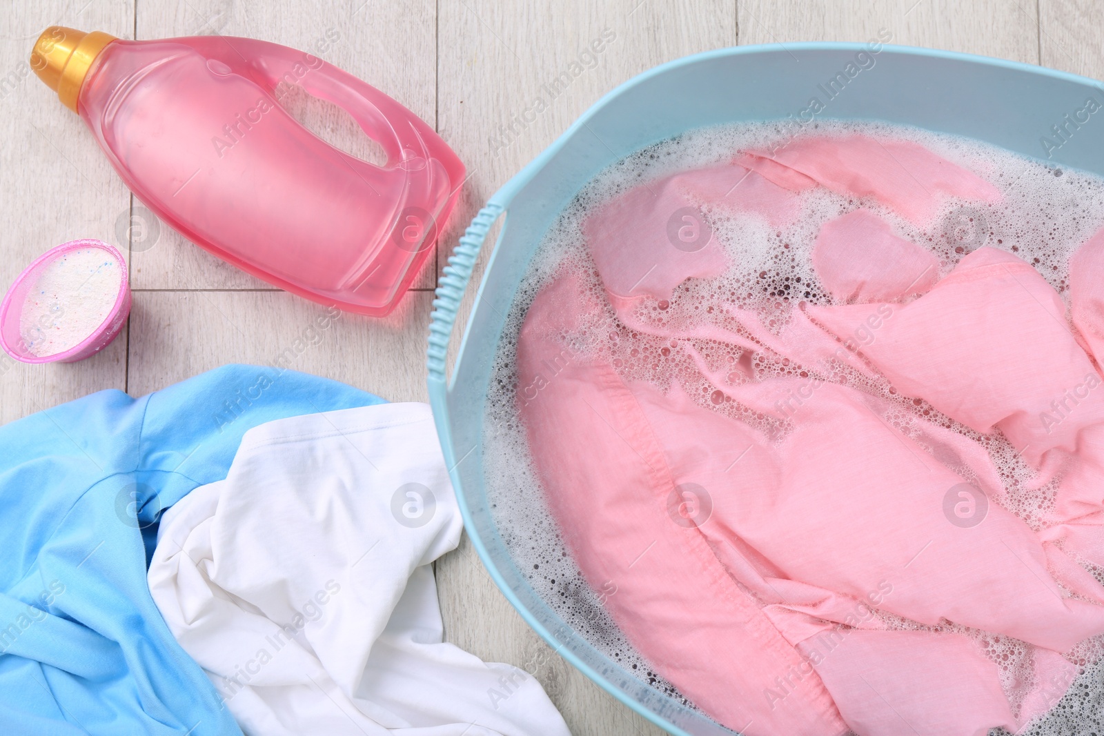 Photo of Basin with pink shirt near bottle of detergent and powder on floor, flat lay. Hand washing laundry