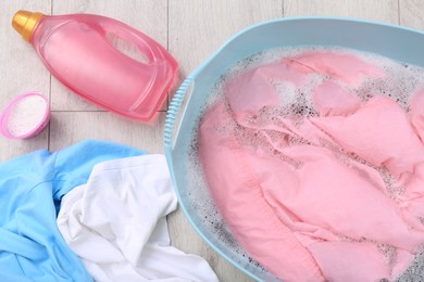 Photo of Basin with pink shirt near bottle of detergent and powder on floor, flat lay. Hand washing laundry