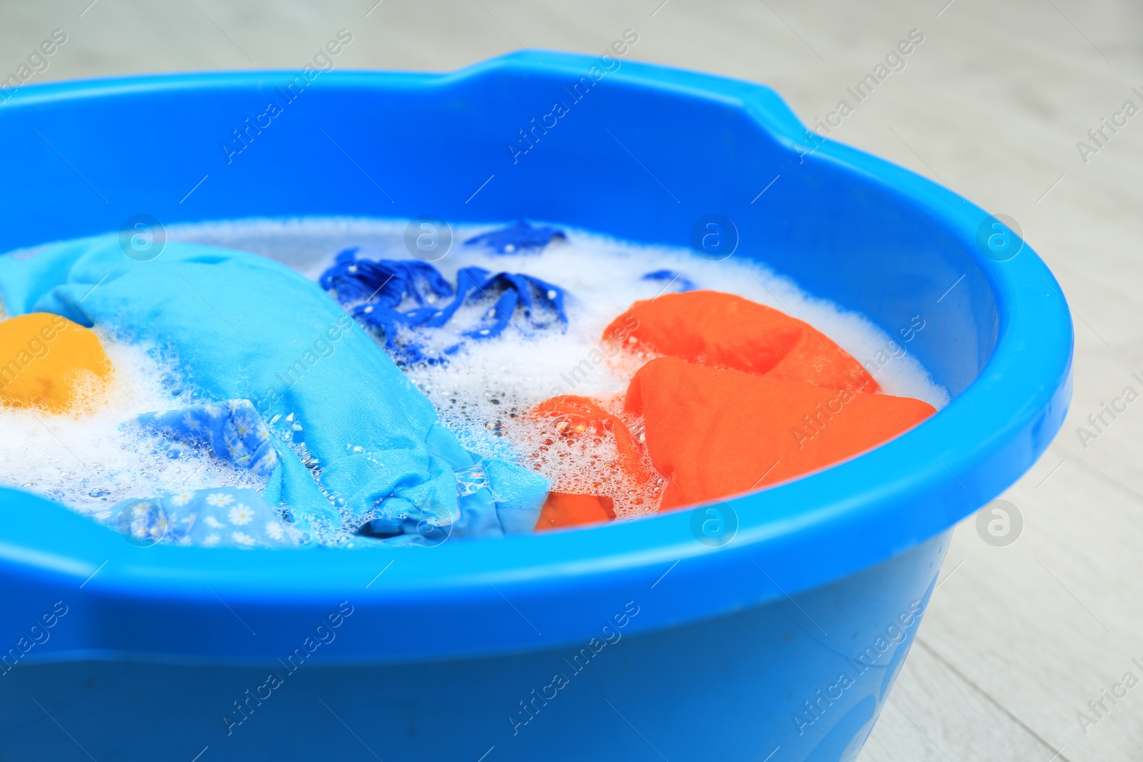 Photo of Basin with colorful clothes on floor, closeup. Hand washing laundry