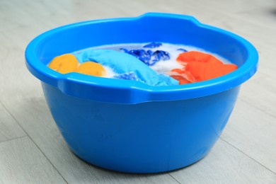 Photo of Basin with colorful clothes on floor, closeup. Hand washing laundry