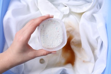 Photo of Woman adding powdered detergent into basin with dirty white clothes, top view