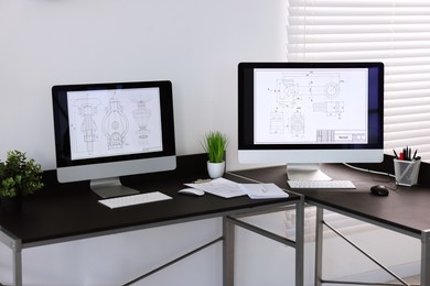 Photo of Modern computers with digital engineering drawing at table in office