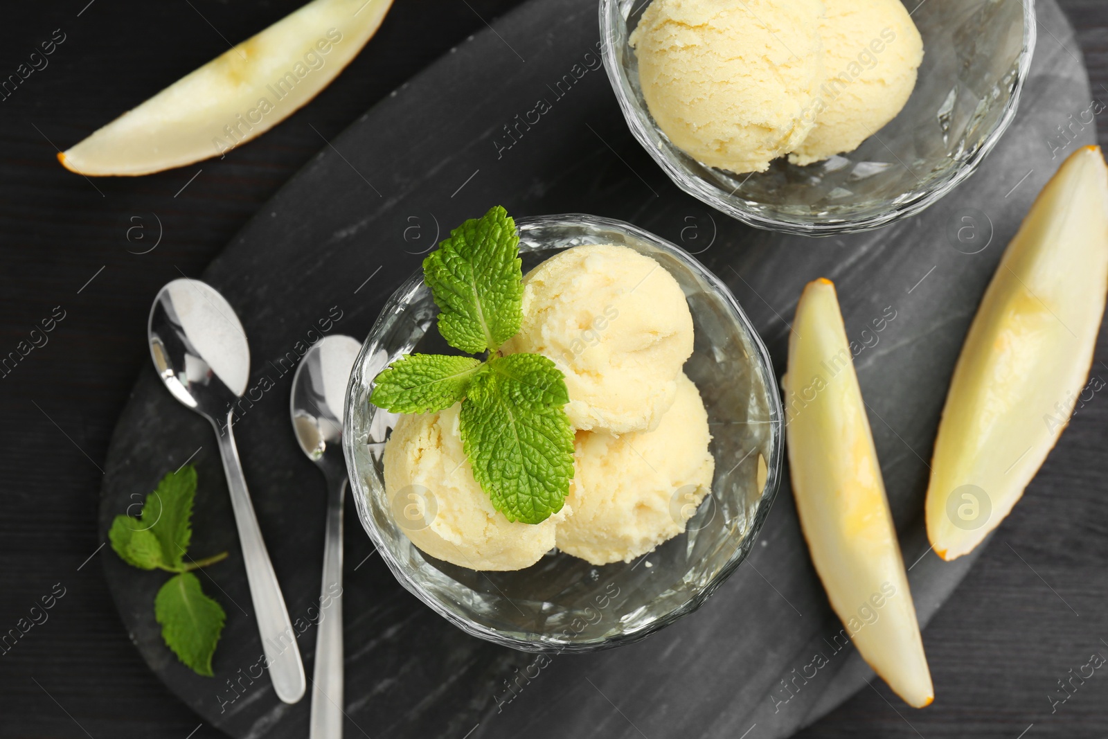 Photo of Scoops of melon sorbet with mint in glass dessert bowls, fresh fruit and spoons on dark wooden table, flat lay