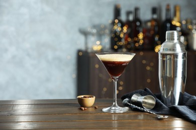 Refreshing cocktail, shaker, jigger, spoon and coffee beans on wooden table. Space for text