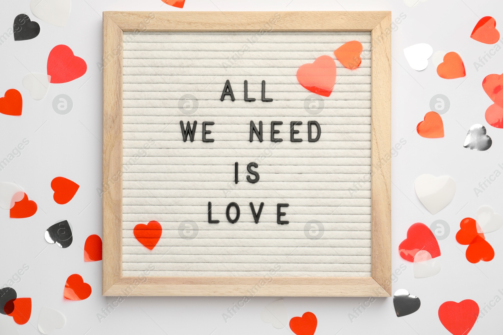 Photo of Letter board with phrase All We Need Is Love and heart shaped confetti on white background, top view