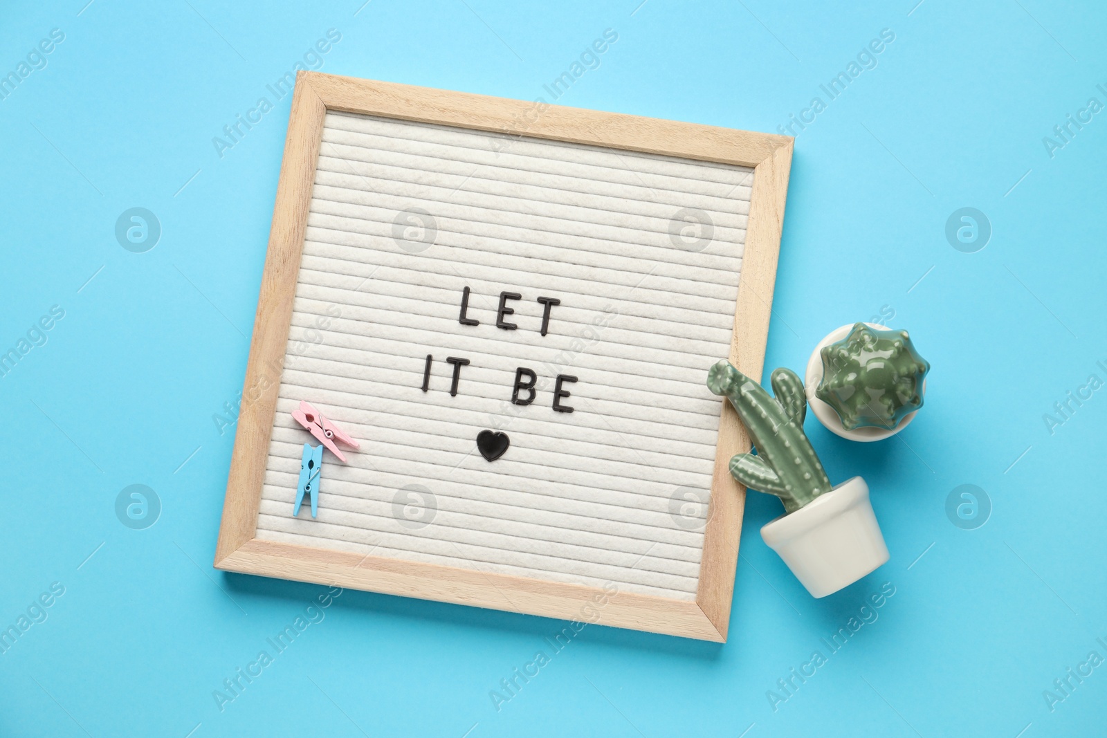 Photo of Letter board with phrase Let It Be, cactus figures and clothes pins on light blue background, flat lay