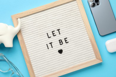 Photo of Letter board with phrase Let It Be, smartphone, glasses, elephant figure and earphones on light blue background, flat lay