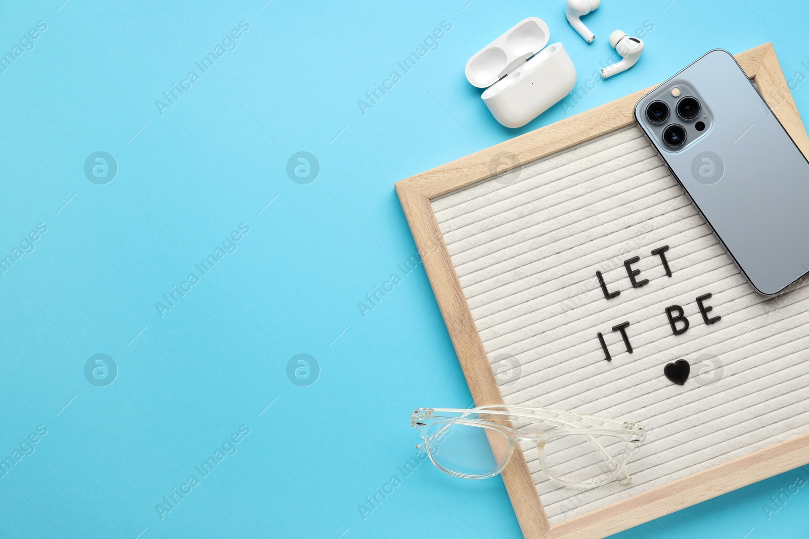 Photo of Letter board with phrase Let It Be, smartphone, glasses and earphones on light blue background, flat lay. Space for text