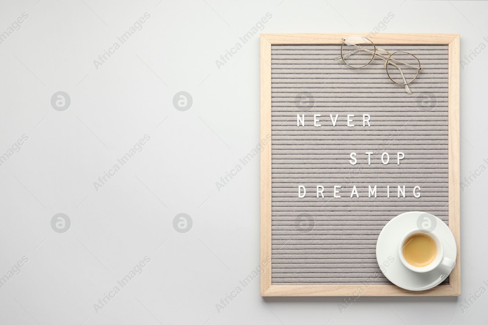 Photo of Letter board with phrase Never Stop Dreaming, glasses and cup of coffee on light table, top view. Space for text