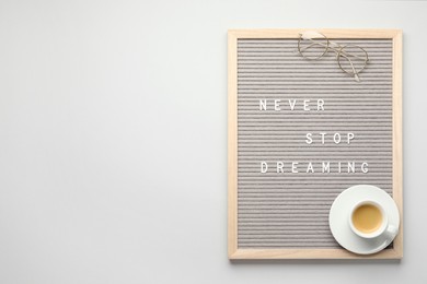 Photo of Letter board with phrase Never Stop Dreaming, glasses and cup of coffee on light table, top view. Space for text