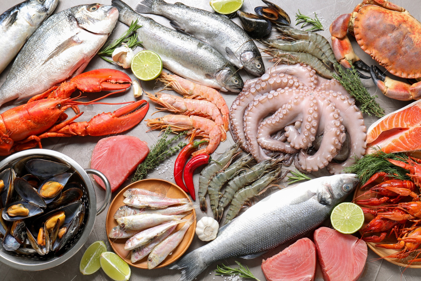 Photo of Many different sea food, herbs and lime on grey table, flat lay