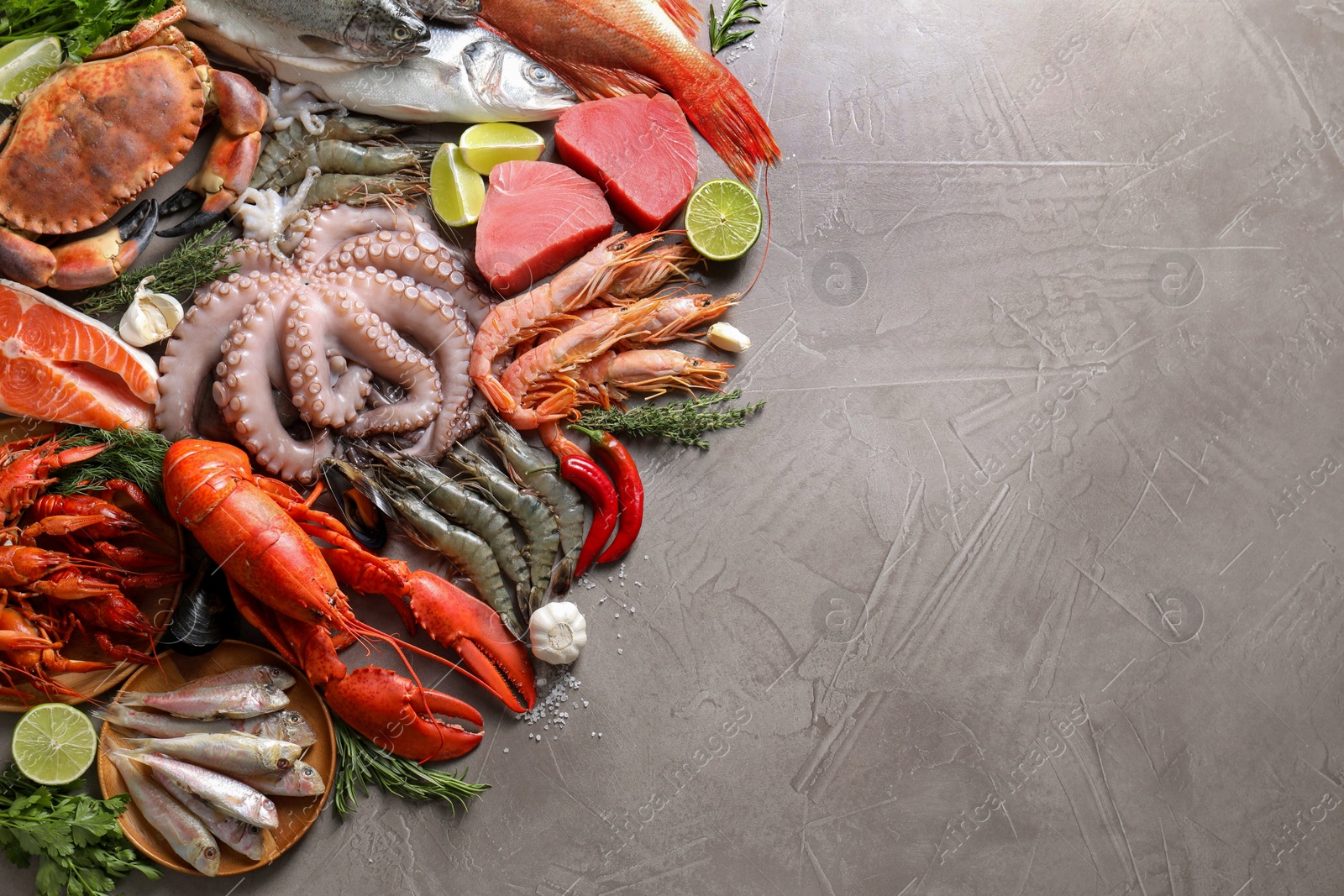 Photo of Many different sea food, herbs, garlic and lime on grey table, flat lay. Space for text