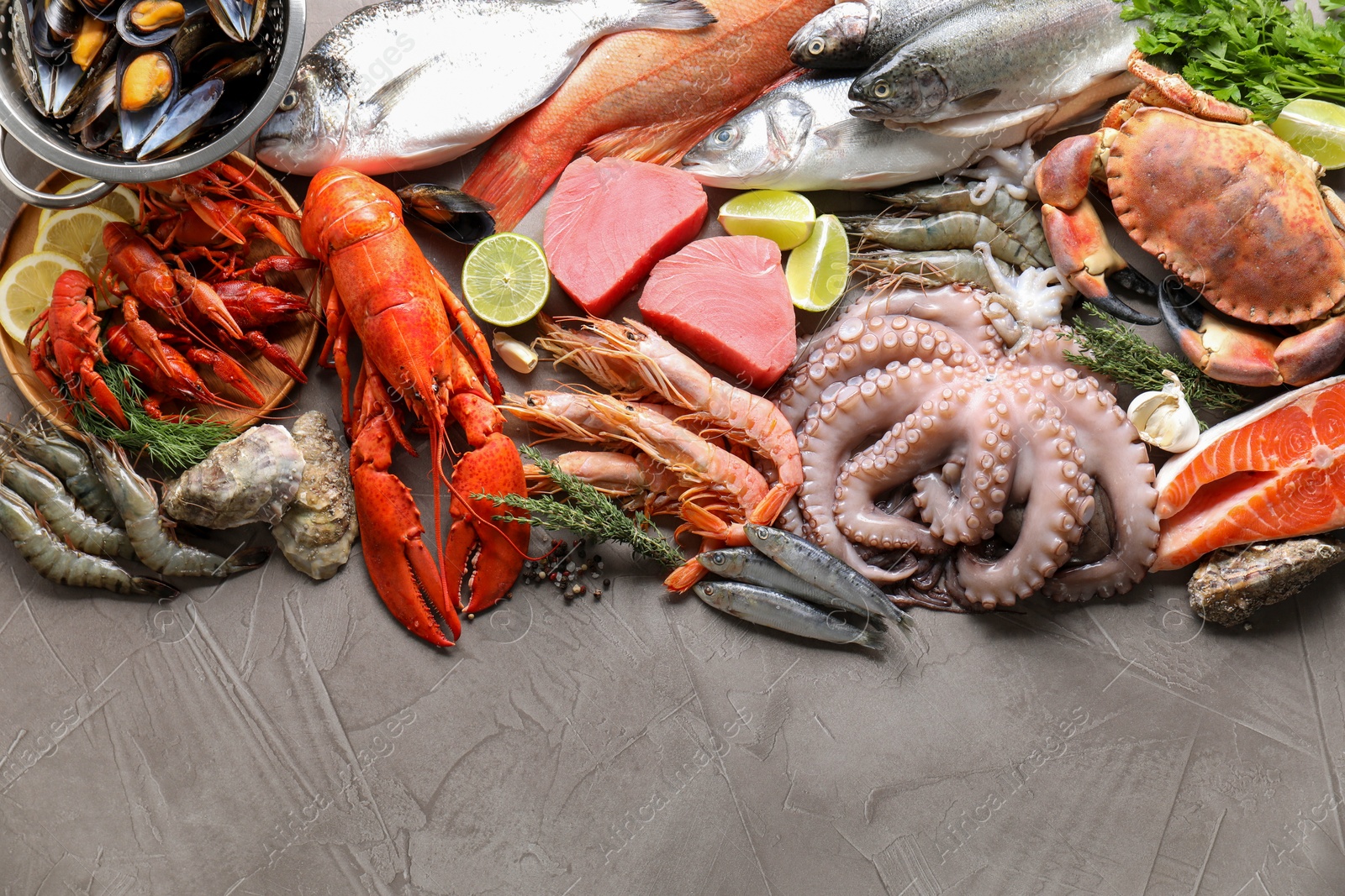 Photo of Many different sea food, herbs and lime on grey table, flat lay. Space for text