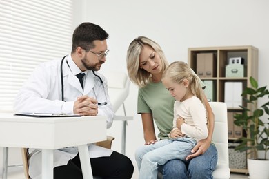 Doctor consulting little girl with stomach pain and her mother in hospital