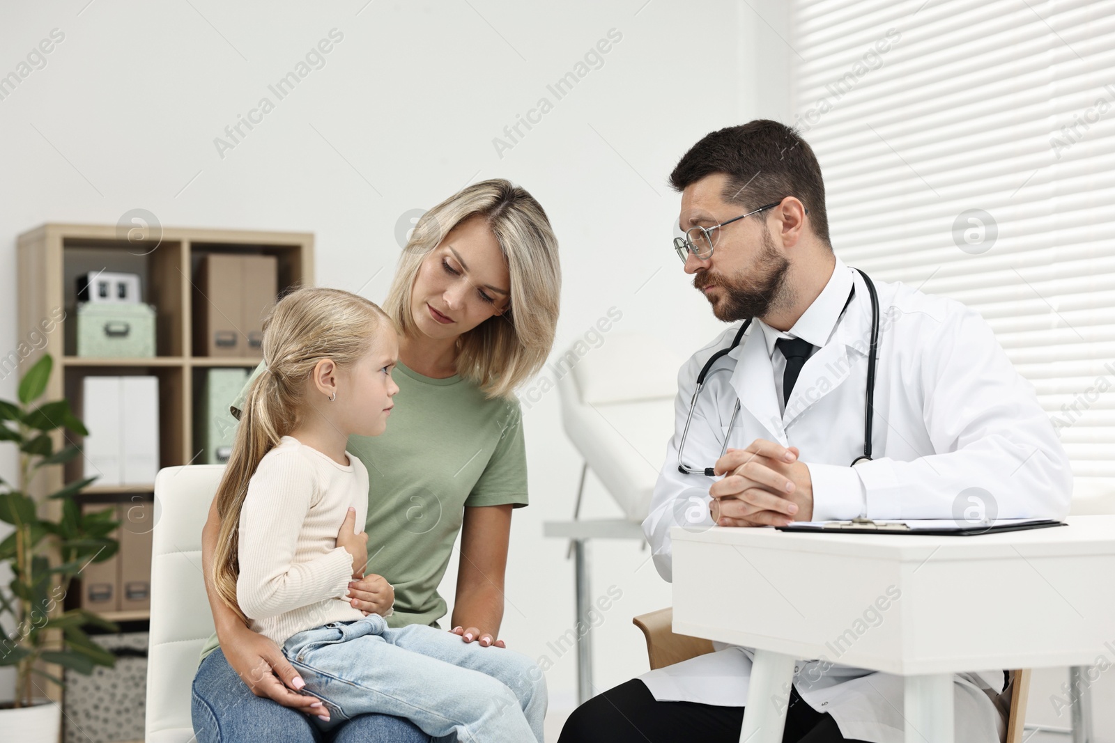 Photo of Doctor consulting little girl with stomach pain and her mother in hospital