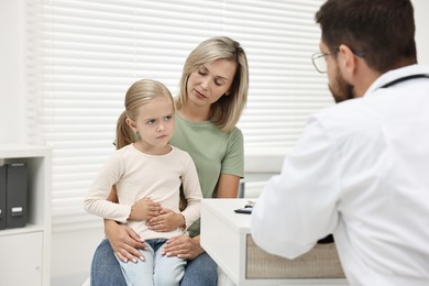 Doctor consulting little girl with stomach pain and her mother in hospital, back view