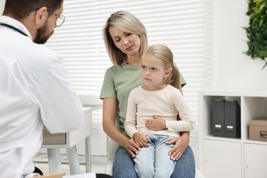 Doctor consulting little girl with stomach pain and her mother in hospital, back view