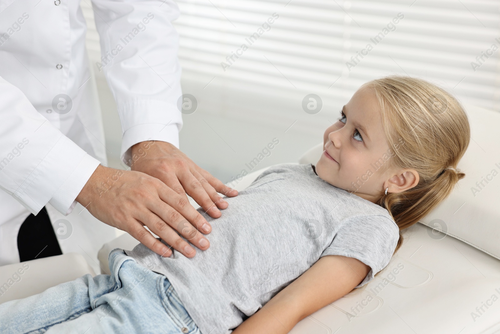 Photo of Doctor examining little girl with stomach pain in hospital, closeup