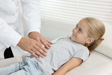 Doctor examining little girl with stomach pain in hospital, closeup