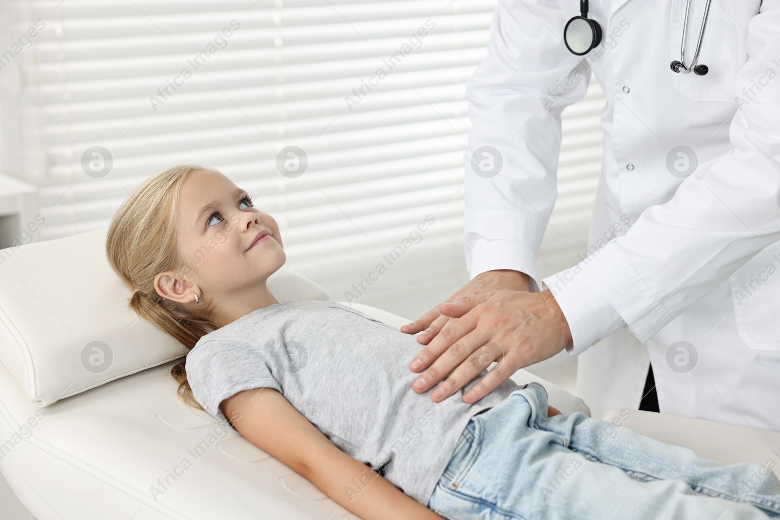 Photo of Doctor examining little girl with stomach pain in hospital, closeup