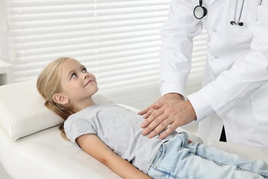 Photo of Doctor examining little girl with stomach pain in hospital, closeup